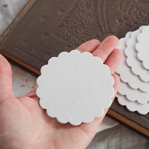 May include: A stack of white scalloped paper circles, perfect for crafting or scrapbooking. The circles are about 3 inches in diameter.