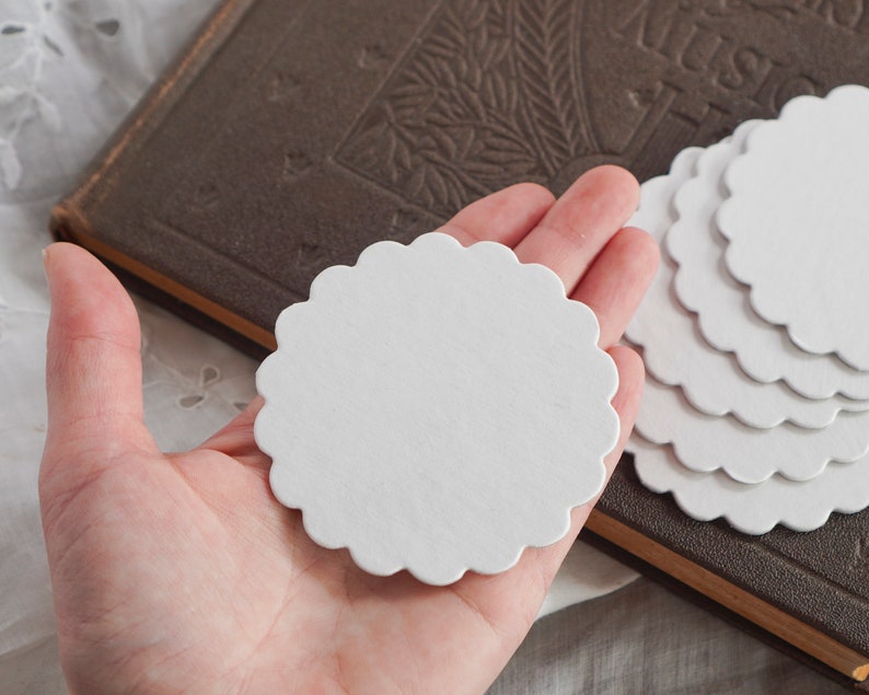 May include: A stack of white scalloped paper circles, perfect for crafting or scrapbooking. The circles are about 3 inches in diameter.