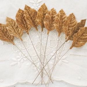 May include: A bunch of ten gold velvet leaves on wire stems. The leaves are arranged in a fan shape and are all facing the same direction.