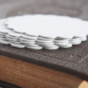 May include: A stack of white paper doilies with scalloped edges, sitting on top of a brown leather-bound book.