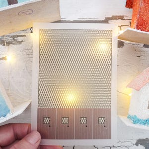 May include: A printable craft template for a miniature house with a brown wood-look base and a black wire mesh pattern on the front. The template has four windows with black frames.