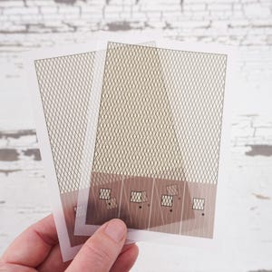 May include: Two sheets of clear plastic with a grid pattern printed on them. The sheets are layered on top of each other and have a brown rectangular area at the bottom with smaller squares printed on it.