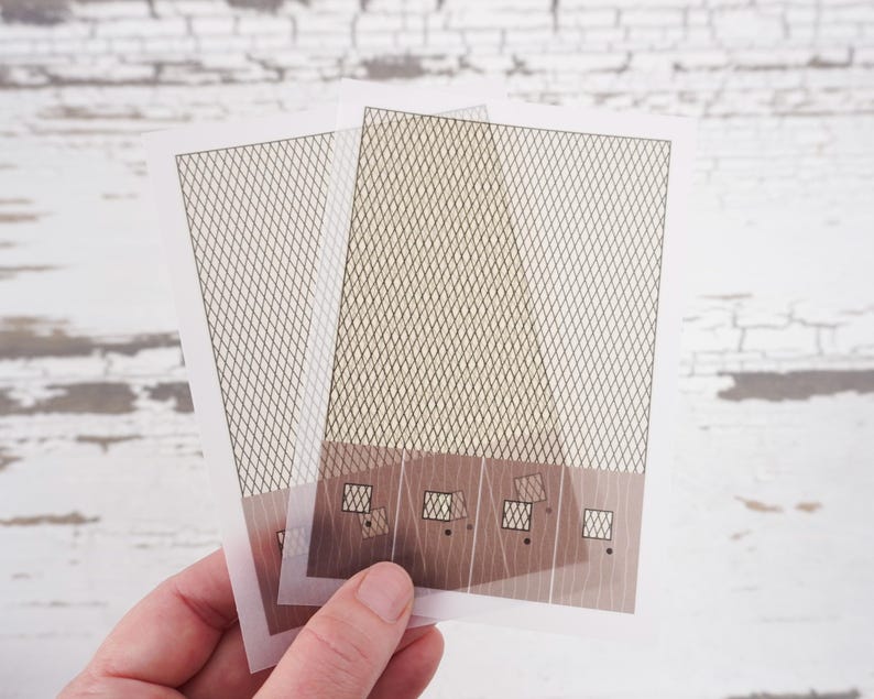 May include: Two sheets of clear plastic with a grid pattern printed on them. The sheets are layered on top of each other and have a brown rectangular area at the bottom with smaller squares printed on it.