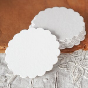 May include: A stack of white scalloped paper circles, perfect for crafting or adding a touch of elegance to your table setting.