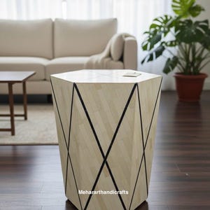 May include: A geometric side table with a light wood finish and black accent lines. The hexagonal table is made of light-coloured wood pieces arranged in a herringbone pattern. The table is approximately 51 cm tall and 46 cm wide.