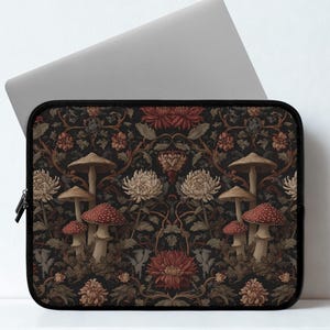 May include: Black laptop sleeve featuring a repeating pattern of mushrooms, flowers, and foliage in shades of brown, red, and cream. The sleeve has a black zipper and a gray laptop is partially visible.