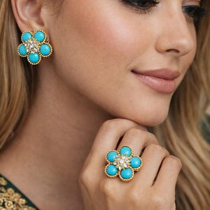Può includere: Set di gioielli a forma di fiore con pietre turchesi e un gruppo centrale di cristalli trasparenti. Il set include orecchini e un anello abbinati con una montatura color oro. Gli orecchini e l'anello sono disegnati con un motivo floreale.