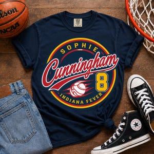 May include: A navy blue short-sleeve t-shirt featuring a circular graphic with the text Sophie Cunningham, the number 8, and Indiana Fever. The design includes a basketball illustration in red, yellow, and white colors on the front of the shirt.