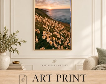 May include: A vertical wall art print featuring a coastal landscape at sunset with a field of white daisies in the foreground, a grassy cliffside, and the ocean under a golden sky. The text reads INSPIRED BY CREATE ART PRINT.