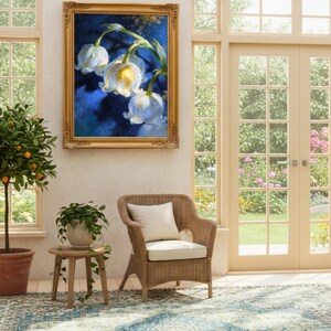May include: A framed floral painting with white flowers and a blue background hangs on a wall. The painting is in a gold ornate frame. A wicker chair with a white cushion sits below the painting. A small wooden table with a potted plant is next to the chair.