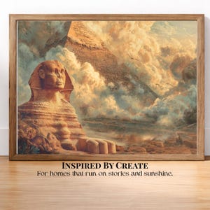May include: A framed wall art print depicting the Great Sphinx and a pyramid set against a cloudy, golden-hued sky. Below the image, the text reads: INSPIRED BY CREATE. For homes that run on stories and sunshine. The frame is a light brown wood.