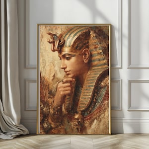 May include: A framed portrait of an Egyptian pharaoh. The artwork depicts a profile view of a person wearing a gold headdress with blue stripes and a cobra. The portrait has a gold frame and is set against a neutral background.