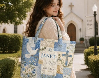 May include: A quilted tote bag featuring a blue and cream patchwork design with a white dove, a blue cross, floral patterns, and the text "JANET" and "God Is Love" printed on the front. The bag has two matching fabric shoulder straps.