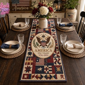 May include: A rectangular table runner featuring a patriotic patchwork design in red, white, and blue. The center displays a circular emblem with a bald eagle, the text AMERICA 250 YEARS 1776-2026, and various geometric star and flag patterns.