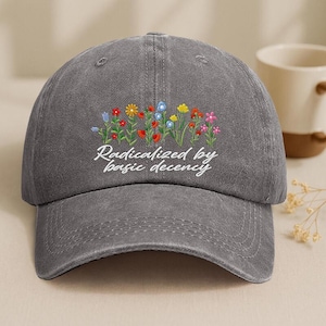May include: Gray baseball cap with embroidered colorful flowers and the text "Radicalized by basic decency." The cap has a curved brim and a classic six-panel design. The flowers include red, yellow, blue, and pink blooms.