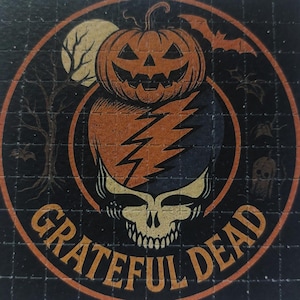 May include: Circular graphic with a Halloween theme. Features a jack-o'-lantern, lightning bolt, skull, and the words "Grateful Dead" in orange. A full moon, bats, and a bare tree are also included in the design. The background is black.