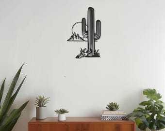 Può includere: Arte da parete in metallo nero raffigurante un paesaggio desertico con un cactus saguaro, montagne e un sole al tramonto. L'opera d'arte è montata su una parete bianca.