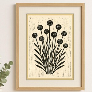 Puede incluir: Impresión botánica en blanco y negro enmarcada. La obra presenta una ilustración estilizada de un grupo de flores con cabezas redondas y punteadas y tallos largos y delgados. La impresión está sobre un fondo crema y enmarcada en madera clara.