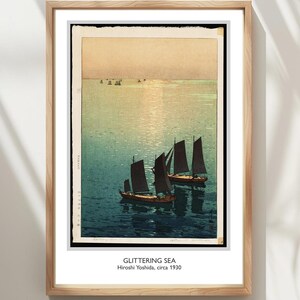 Pode incluir: Impressão emoldurada de uma obra de arte intitulada "Glittering Sea" de Hiroshi Yoshida, por volta de 1930. A obra retrata barcos com velas escuras em um mar azul-esverdeado cintilante sob um céu dourado. A impressão está em uma moldura de madeira.