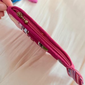 Puede incluir: Una bolsa con cremallera de color magenta con un extremo decorativo. La bolsa tiene una cremallera dorada y un acento de tela estampada. La bolsa est&aacute; dise&ntilde;ada con una est&eacute;tica colorida y caprichosa.