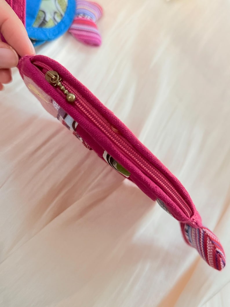Puede incluir: Una bolsa con cremallera de color magenta con un extremo decorativo. La bolsa tiene una cremallera dorada y un acento de tela estampada. La bolsa est&aacute; dise&ntilde;ada con una est&eacute;tica colorida y caprichosa.