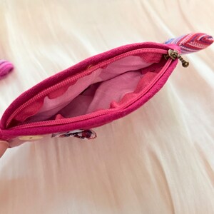 Puede incluir: Un estuche con cremallera de color rosa brillante con una leng&uuml;eta de tela estampada. El estuche est&aacute; abierto, revelando un forro interior rosa claro. El exterior es de un rosa s&oacute;lido y vibrante.