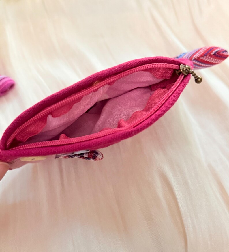 Puede incluir: Un estuche con cremallera de color rosa brillante con una leng&uuml;eta de tela estampada. El estuche est&aacute; abierto, revelando un forro interior rosa claro. El exterior es de un rosa s&oacute;lido y vibrante.