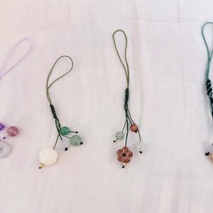 Puede incluir: Cuatro colgantes decorativos con detalles de cuentas y cordones en bucle. Los colgantes presentan varios colores, incluyendo morado, verde y rosa, con elementos florales y esféricos. Los cordones son en tonos verdes y morados.