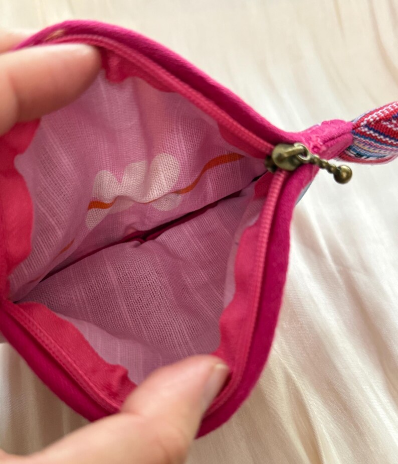 Puede incluir: Una bolsa con cremallera de color rosa intenso con un interior estampado. La tela interior presenta un dise&ntilde;o floral blanco con detalles en naranja. La cremallera es de color lat&oacute;n y la bolsa tiene un peque&ntilde;o lazo de tela con un estampado colorido.