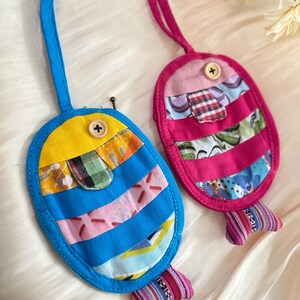 Puede incluir: Dos adornos artesanales de tela con forma de pez. Uno es azul y amarillo, el otro rosa. Ambos tienen cuerpos a rayas, detalles de botones y aletas caudales estampadas. Tienen un lazo para colgar.