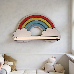 Pode incluir: Uma prateleira de madeira em forma de arco-íris com um design de arco vermelho, amarelo, azul e azul claro. A prateleira é suportada por dois suportes em forma de nuvem e tem uma prateleira retangular. A prateleira é montada numa parede azul clara.