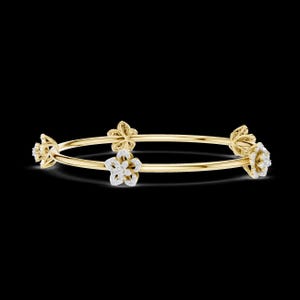 May include: A gold bangle bracelet with four flower designs. Each flower is adorned with small, sparkling white gemstones. The bracelet has a simple, elegant design, perfect for adding a touch of sophistication to any outfit.