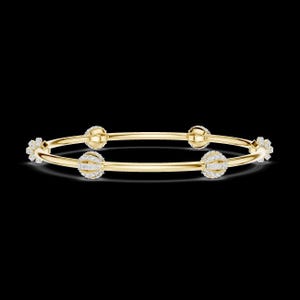 May include: A gold-colored bangle bracelet with four decorative, spherical elements encrusted with small, sparkling stones. The bracelet has a simple, elegant design, with a flower-shaped accent on each end. The background is black.