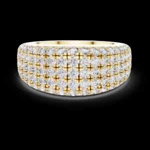 May include: A wide, gold-toned ring encrusted with multiple rows of sparkling, clear gemstones. The ring has a rounded shape and a polished finish, reflecting light against a dark background. The gemstones are evenly spaced, creating a dazzling effect.