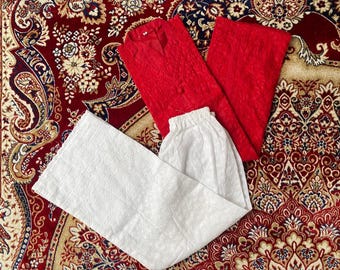 Puede incluir: Una camisa roja y pantalones a juego se muestran con un pantalón blanco sobre una alfombra estampada. El conjunto rojo tiene una apariencia texturizada. Los pantalones blancos tienen un diseño detallado en relieve.