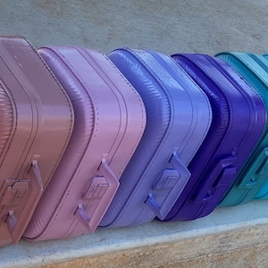May include: A row of colorful suitcases lined up in a rainbow pattern. The suitcases are all the same size and shape, and they are made of a hard, plastic material.