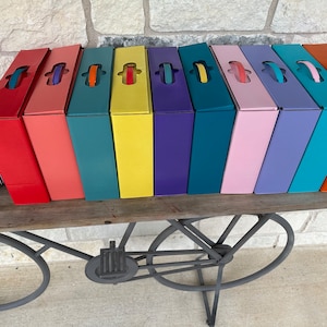 May include: A row of ten colorful boxes with handles, arranged in a rainbow pattern on a wooden shelf. The shelf is attached to a metal bicycle stand.