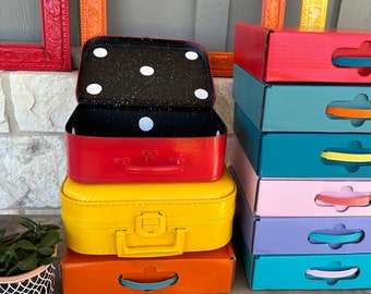 500 paperboard suitcases in 7 different colors painted a solid color Approx. 12" × 8" x 3.5" hand painted with black interior white dots