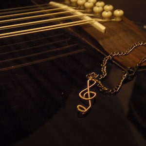 Könnte beinhalten: Ein goldener Musiknoten-Anhänger hängt an einer Kette an einer schwarzen Akustikgitarre.