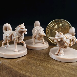 May include: Three beige dog figurines on circular bases. The dogs are in various poses, with detailed features and harnesses. A gold coin is in the background. The figurines are likely made of resin.