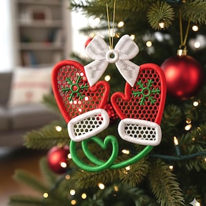 Könnte beinhalten: Ein Weihnachtsbaumschmuck mit zwei roten Fäustlingen mit weißen Verzierungen und grünen Schneeflockenmustern. Über den Fäustlingen befindet sich eine weiße Schleife, und ein grünes herzförmiges Design verbindet sie. Der Schmuck hängt an einem goldenen Faden.
