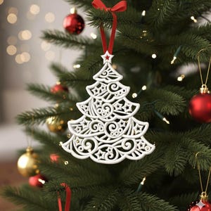 Könnte beinhalten: Weißer, aufwendig gestalteter Weihnachtsbaumschmuck mit rotem Band und Sternendetail, der an einem geschmückten Weihnachtsbaum hängt. Das Ornament hat ein detailliertes, durchbrochenes Design mit Wirbeln und Sternformen.