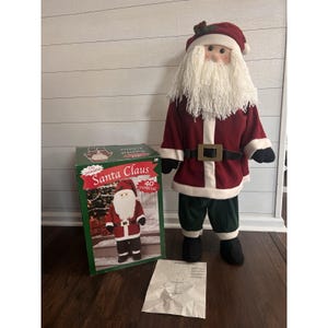 May include: A 40-inch tall Santa Claus figure with a red suit, white beard, and black boots stands next to a box with the words "Santa Claus" on it. The figure has a red hat and a black belt with a gold buckle. The box shows a picture of the Santa Claus figure.