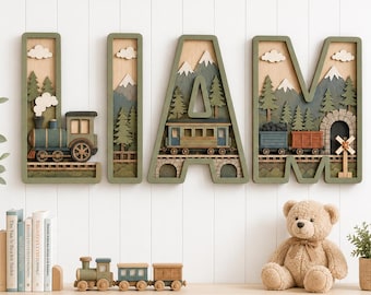 May include: Four large wooden letters spelling LIAM, each featuring a layered 3D scene with a train, pine trees, mountains, and clouds. The letters are mounted on a wall above a shelf containing a small toy train, books, and a teddy bear.