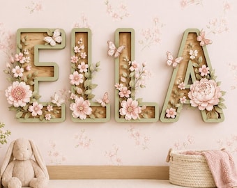 May include: Four large, sage green wooden letters spelling ELLA, each featuring a natural wood interior. The letters are decorated with various pink flowers, green leaves, and small butterflies. The letters are mounted on a light pink floral wall.