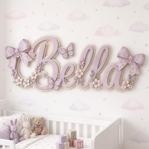 May include: A wall-mounted wooden sign displaying the name Bella in large, light purple script letters. The sign is decorated with two large fabric bows on the ends, several small pink and white floral accents, and two purple butterfly cutouts.