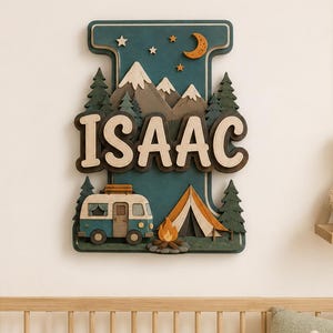 May include: A layered wooden wall sign shaped like the letter I, featuring a dark teal background with a mountain range, pine trees, a camper van, a tent, and a campfire. The name ISAAC is displayed in large, cream-coloured 3D block letters.