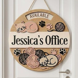 May include: A round wooden door sign featuring a light wood finish, a hanging rope, and the text "AVAILABLE" and "Jessica's Office". The design includes layered cutouts of sleeping cats, yarn balls in shades of pink and black, and paw prints.