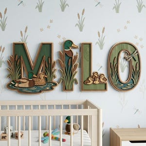 May include: A set of four wooden wall letters spelling the name MILO, featuring a layered design with green backgrounds, brown cattails, and mallard ducks. The letter M shows two ducks, the I features a duck head, the L has ducklings, and the O includes a dragonfly.