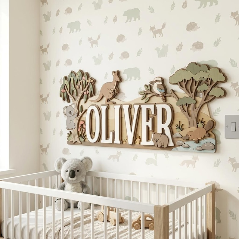 May include: Wooden name sign with the name "OLIVER" in white letters, featuring Australian animals like a kangaroo, koala, and platypus. The sign is set against a backdrop of a nursery with a crib and animal-themed wallpaper.